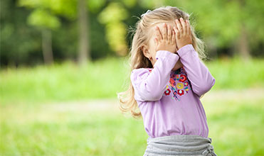 a child playing hide and seek outside with her parents girl playing hide and seek