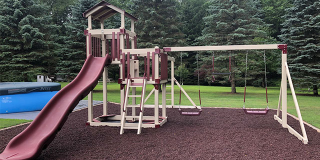 home swing set with a slide, swings, overhead climbers, and red rubber playground mulch color coordinated home swing set